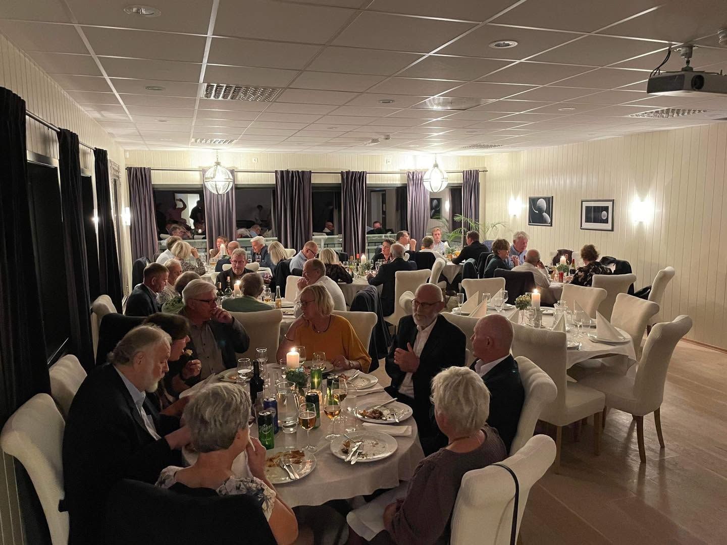 Fullsatt selskapssal med gjester ved runde bord og levende lys